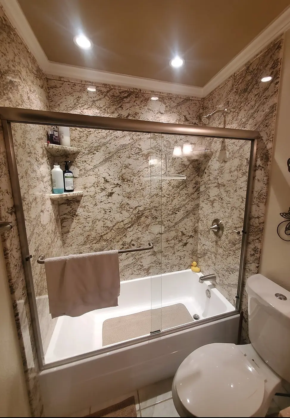Granite-Look Tub Surround — warm granite-look tub surround with corner shelves, brushed nickel trim and a bypass glass door over a soaking tub, installed by Revive Bath Solutions in Lindale, TX