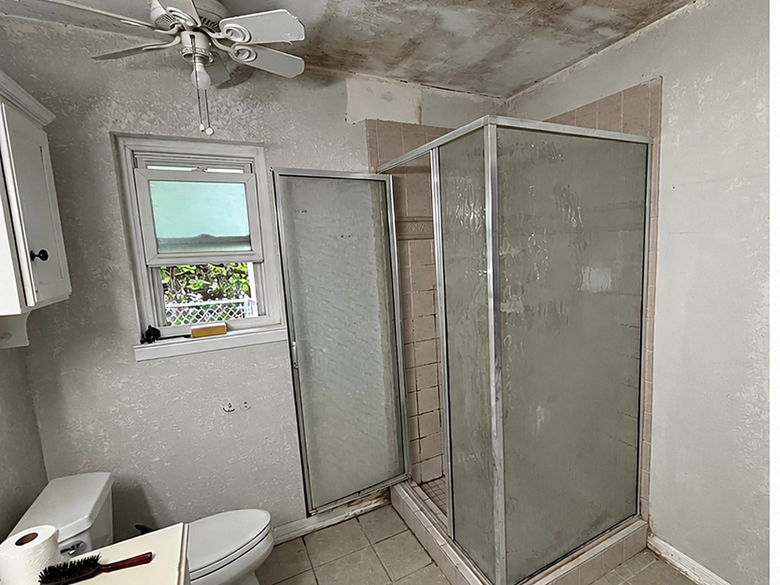 Before: dated corner tile shower with cloudy glass doors and heavy mold staining across the bathroom ceiling in Tyler, TX