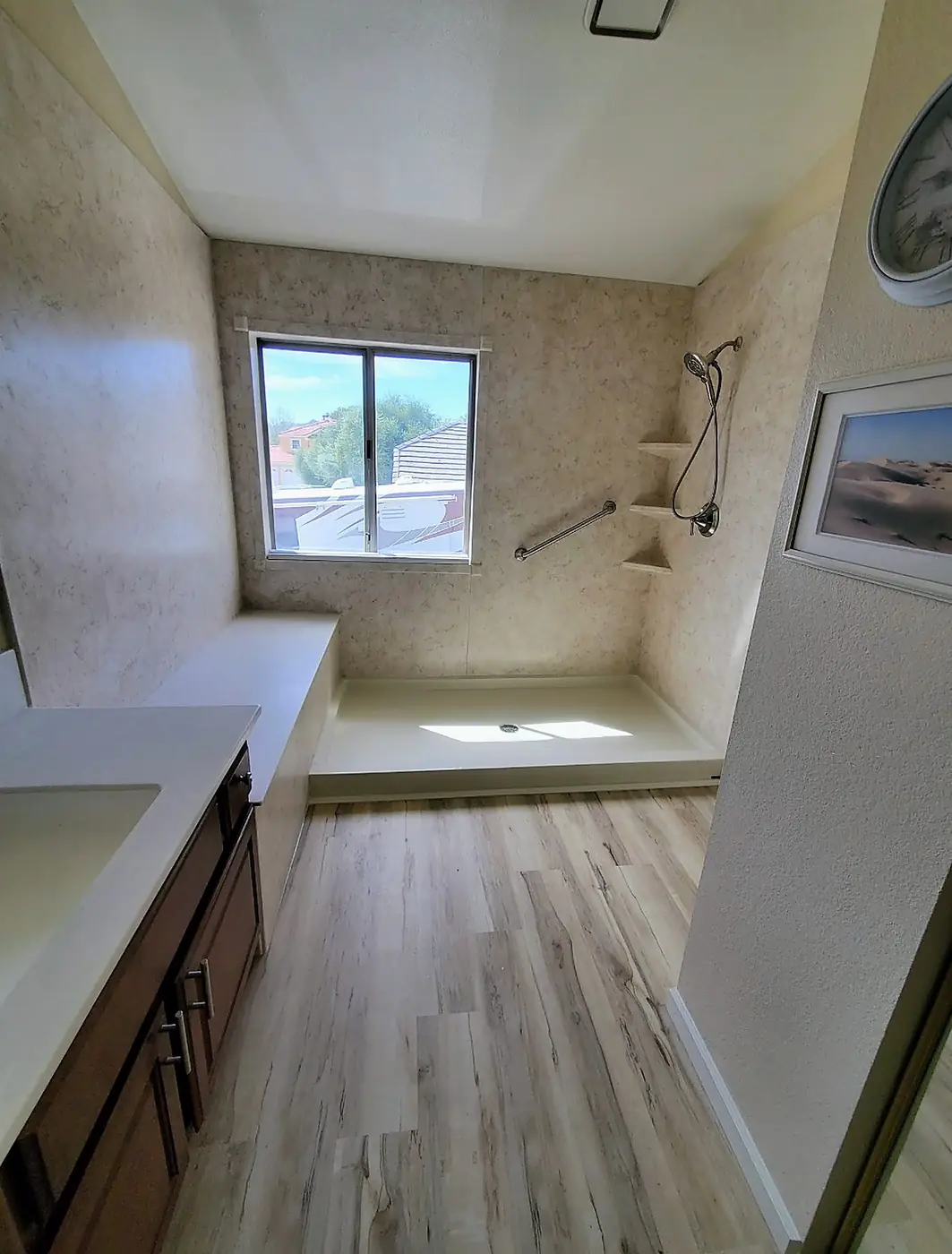 Travertine Curbless Shower — curbless travertine-look shower with a full-length bench, corner shelves, grab bar and wood-look luxury vinyl flooring, installed by Revive Bath Solutions in Longview, TX