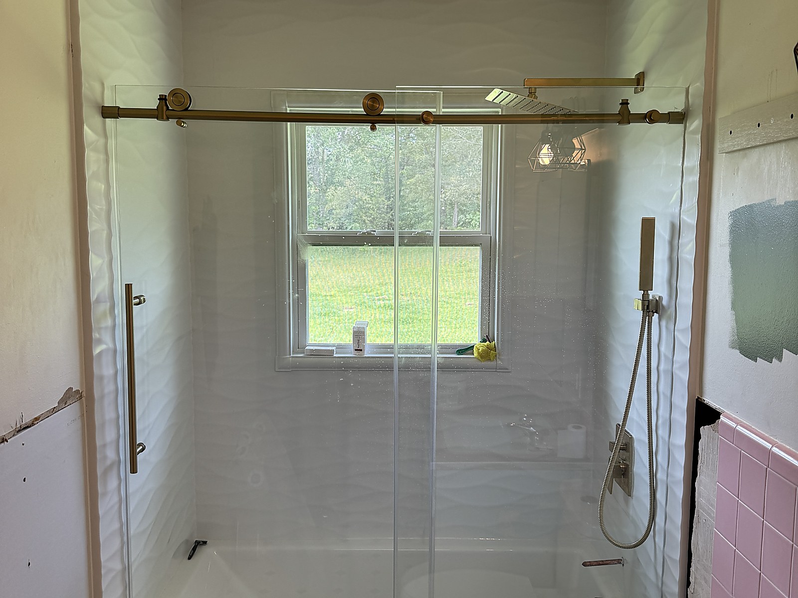 After: wave-textured grout-free wall panels with brushed gold sliding glass hardware and a rainfall shower head installed by Revive Bath Solutions in Lindale, TX