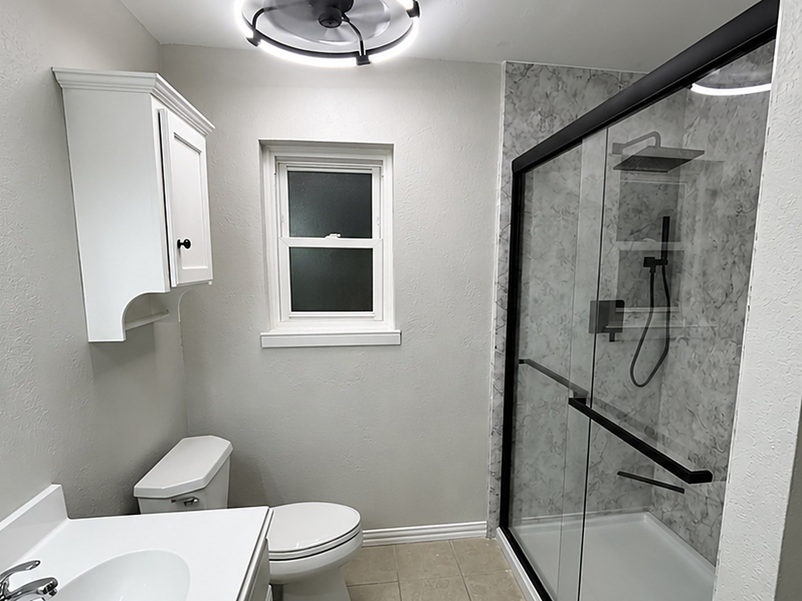 After: grout-free marble-look shower panels with a black-framed sliding glass door, fresh grey paint and a modern ring light, remodeled by Revive Bath Solutions in Tyler, TX