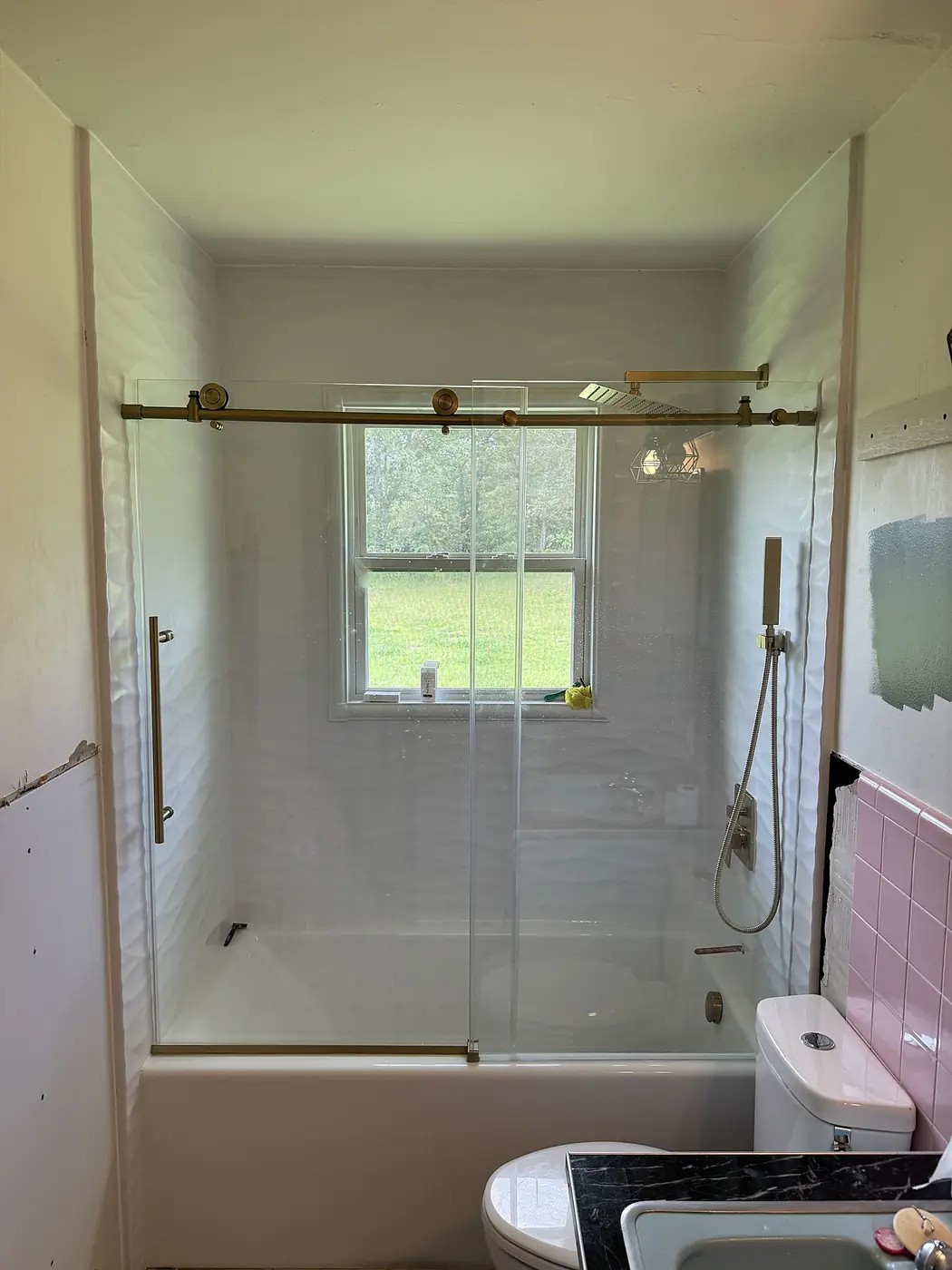 Wave Panel Tub & Shower — textured wave-pattern white wall panels with brushed gold sliding glass hardware, rainfall head and hand shower over a new tub, installed by Revive Bath Solutions in Lindale, TX