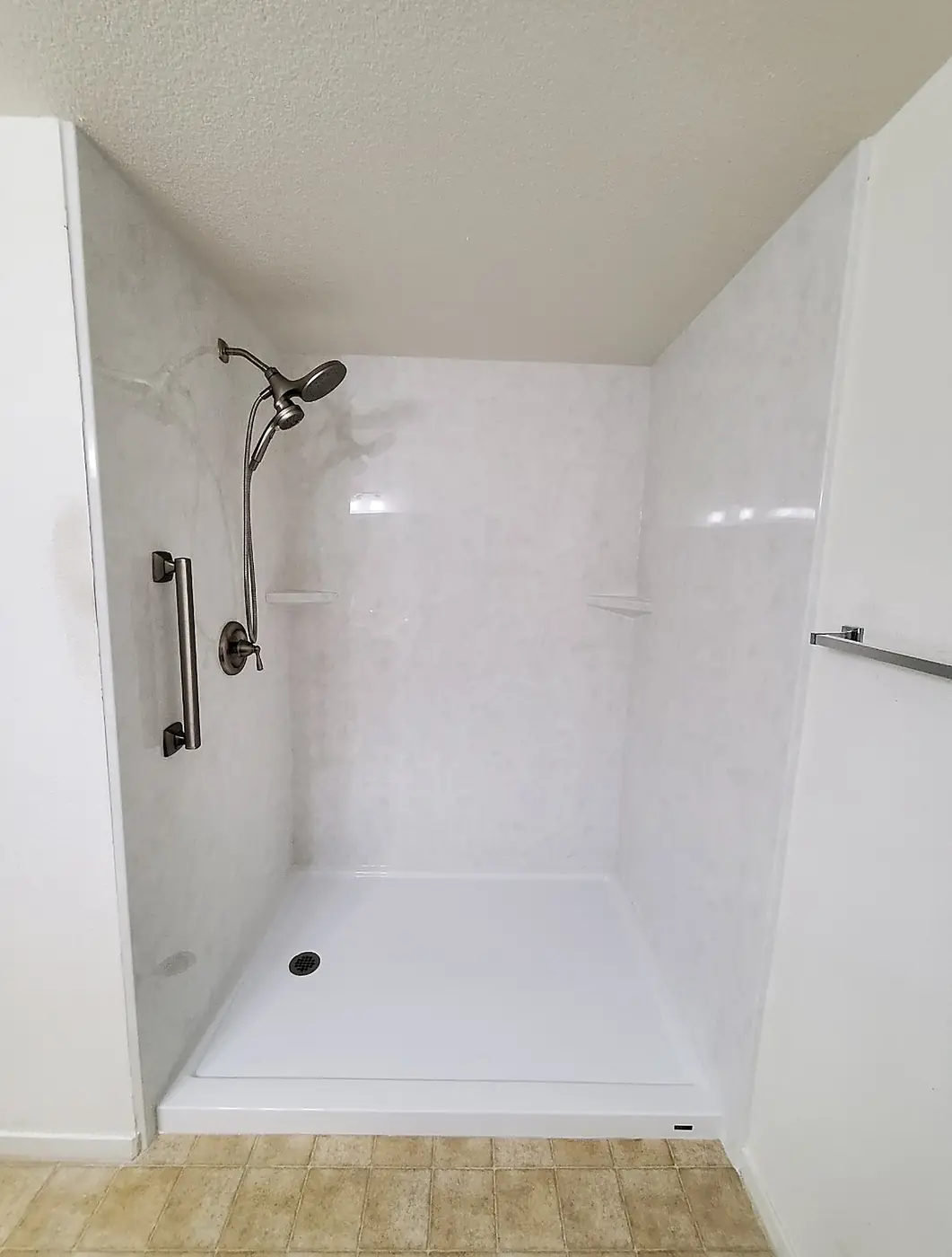 Barrier-Free White Shower — seamless white marble-look shower with a low-threshold pan, brushed nickel grab bar, slide bar and hand shower, installed by Revive Bath Solutions in Canton, TX